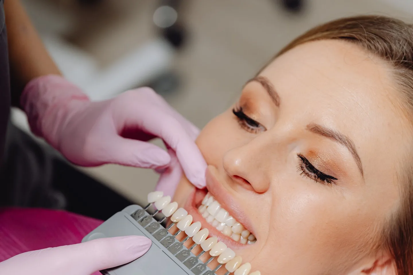 Dental professional holding a physical shade guide beside a patient's teeth