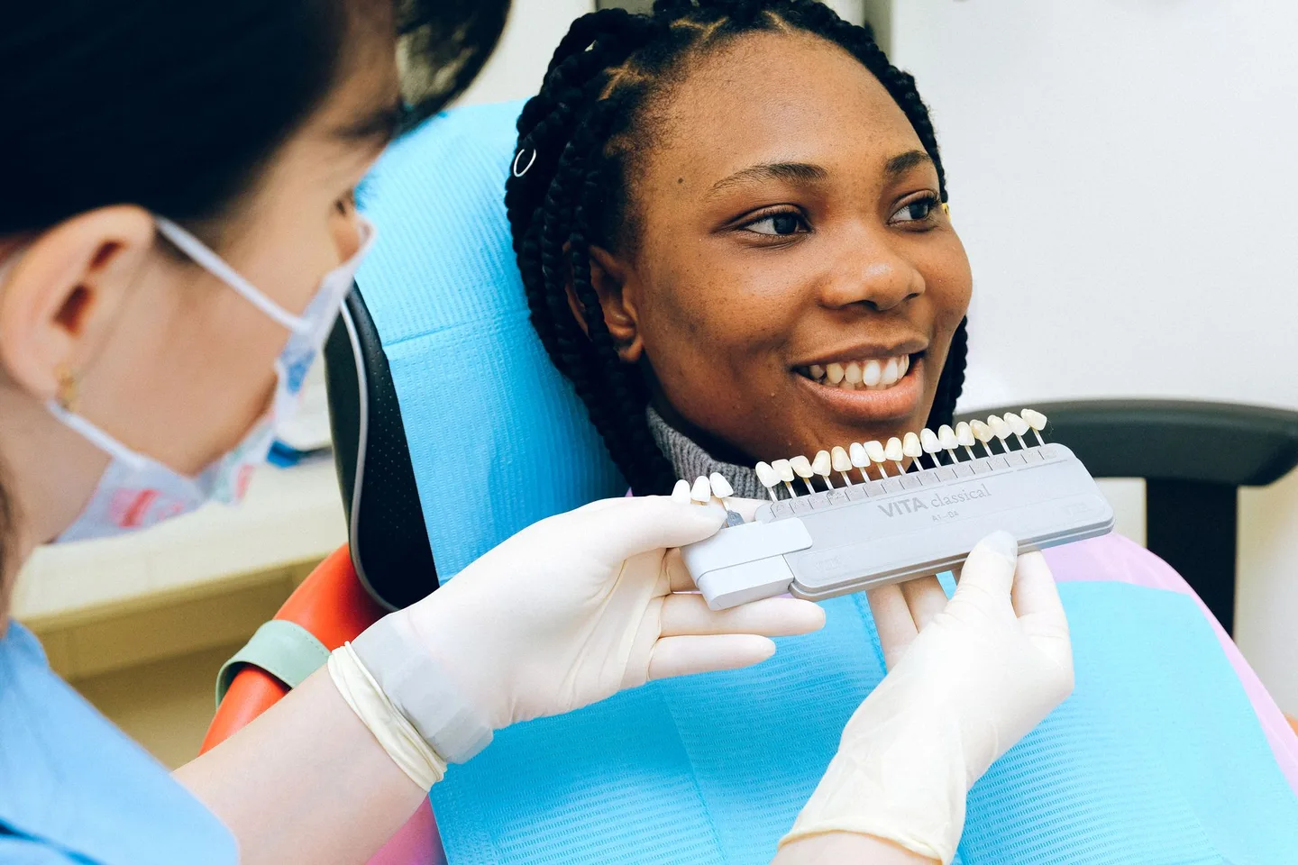 Smiling patient comparing a physical tooth shade guide with a dental professional
